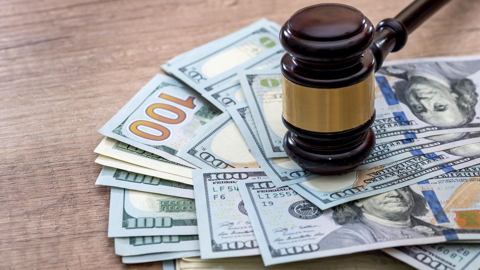 A judge’s gavel resting on a fan of $100 bills