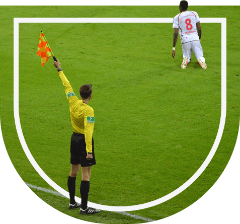 A referee holding up the flag in front of a soccer player.