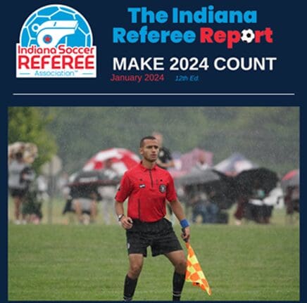 A referee is standing in the grass with his flag.